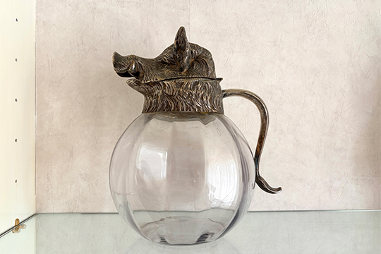 1 CARAFFA ROTONDA IN CRISTALLO CON VERSATOIO E MANICO DECORO CINGHIALE IN METALLO COLORE ARGENTO DIM. 17x27 CM